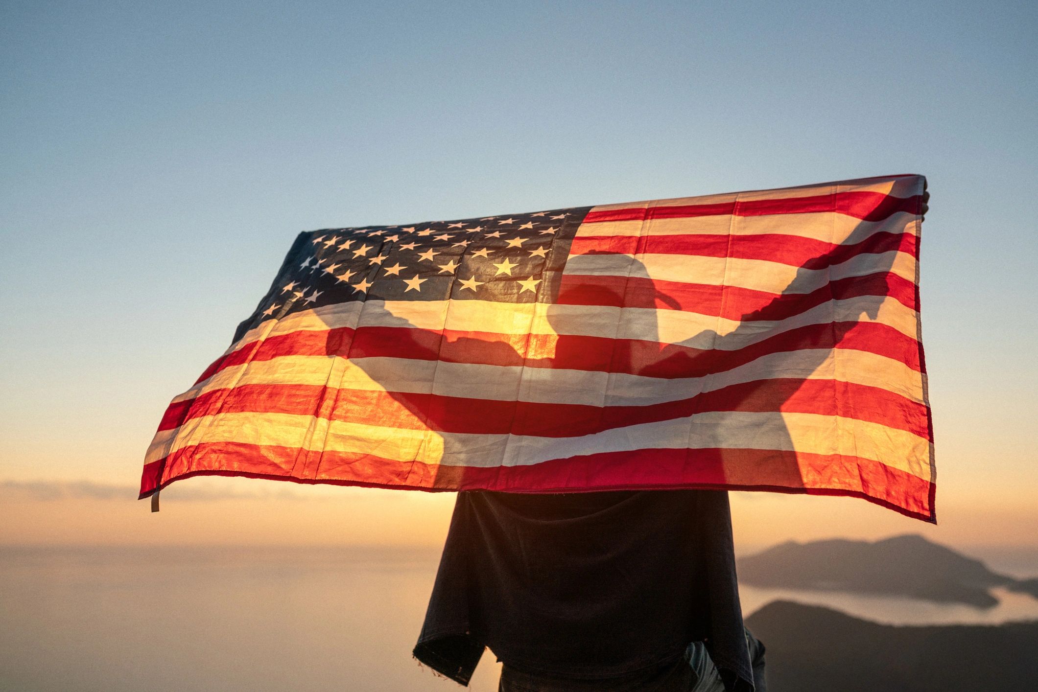 Proud man raising the flag of the United States of America at sunset