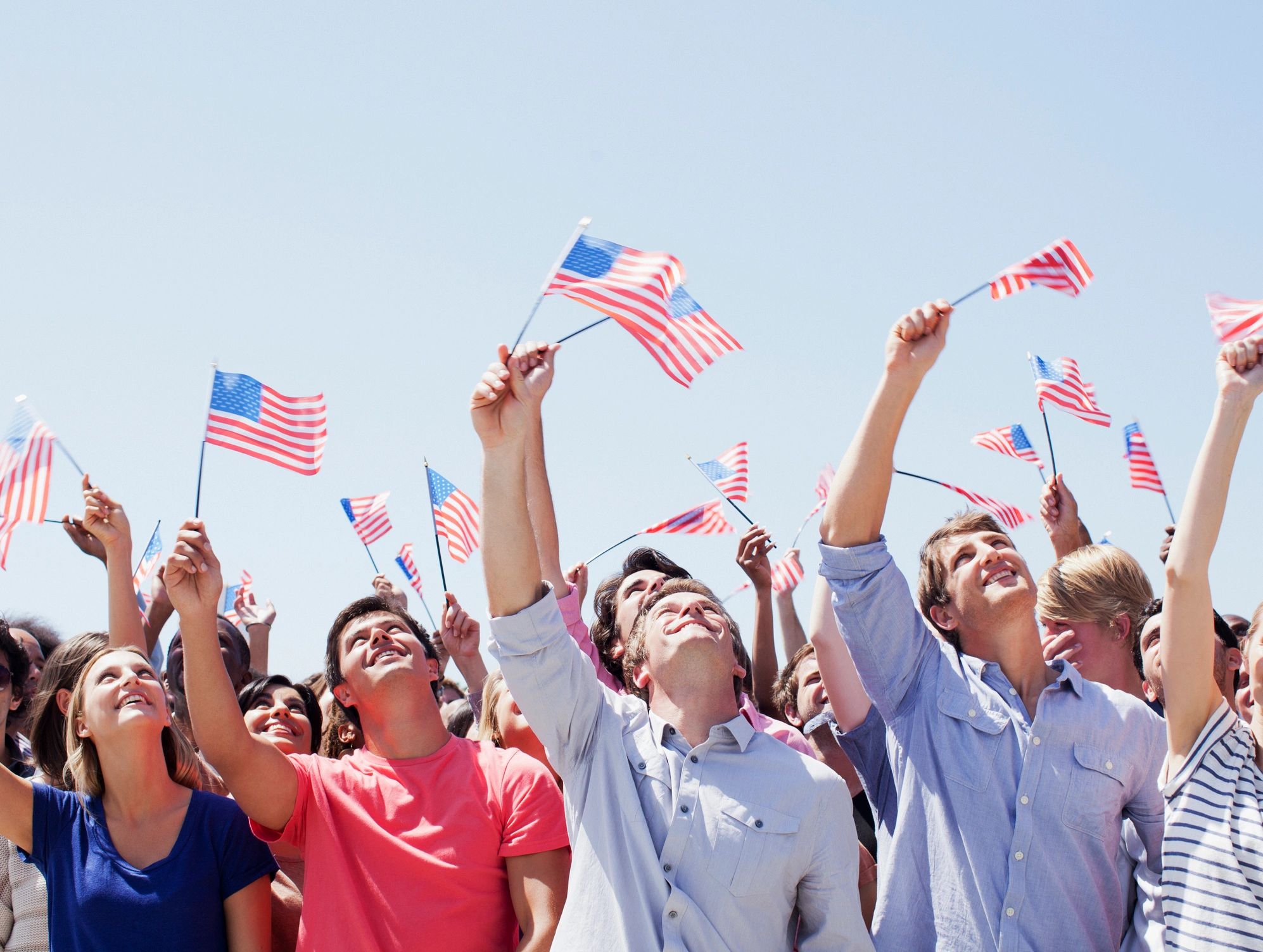 Smiling crowd waving American flags during a patriotic public event